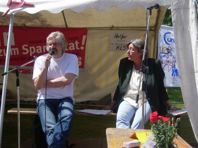 Mit Mikrofon: Axel Köhler-Schnura. Neben ihm hört Anne Frohnweiler, Vorsitzende der DKP Rheinland-Westfalen,  aufmerksam zu.