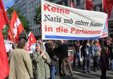 Mai-Demo mit roten Fahnen und Transparent: Keine Nazis und andere Rassisten in die Parlamente!