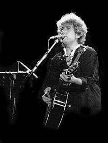 Bob Dylan am Mikrofon mit Gitarre.