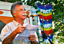 Leo Mayer am Mikrofon, im Hintergrund Friedensfahnen.