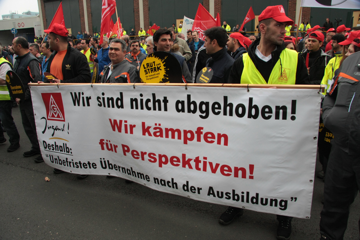 Demonstranten mit roten IG-Metall-Fahnen und Transparent mit dem Logo der IG Metall Jugend: »Wir sind nicht abgehoben. Wir kämpfen für Perspektiven! Deshalb: Unbefristete Übernahme nach der Ausbildung«